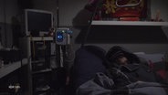 Eine von ME/CFS betroffene Patientin, die nur im Dunkeln liegen kann. Um ihr Bett sind Geräte wie im Krankenhaus zu sehen. © Screenshot 