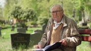 Leo Thiel sitzt auf einer Bank auf einem Friedhof. © Screenshot 