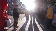 Menschen bei einem Rundgang durch ein Stadtgebiet stehen im Sonnenuntergang vor einem Stolperstein. © Screenshot 