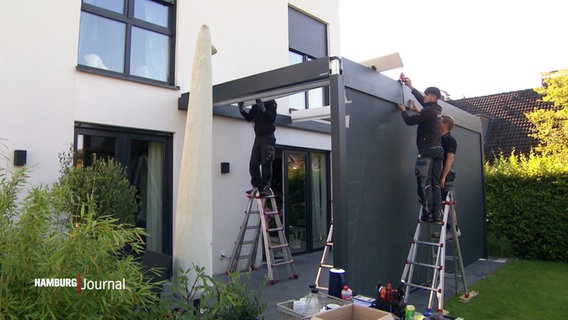 Drei Handwerker stehen auf Leitern und arbeiten an einem Haus. © Screenshot 