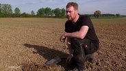 Ein Landwirt kniet auf einem trockenen Acker. © Screenshot 