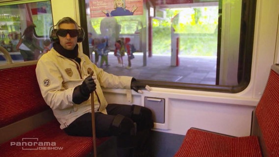Michel Abdollahi in einem Altersanzug in der S-Bahn.  