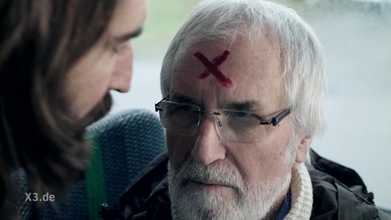 Auf dem Kopf eines älteren Mannes steht ein X in Rot geschrieben.  