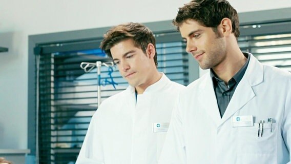 Zwei junge Ärzte stehen nebeneinander in einem Krankenhauszimmer. © NDR 