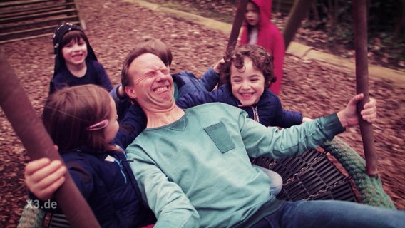 Dennis Kaupp auf einer Schaukel mit Kindern  