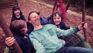 Dennis Kaupp auf einer Schaukel mit Kindern  