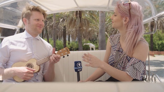 Sloweniens ESC-Kandidaten Lea Sirk und Moderator Stefan Spiegel sitzen zusammen im Tuk Tuk.  