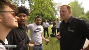Ein Polizeibeamter spricht mit drei jungen Männern, die den Vatertag feiern. © NDR 