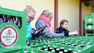 Drei Menschen streichen das Wort "bekömmlich" von Bierflaschen-Aufklebern.  