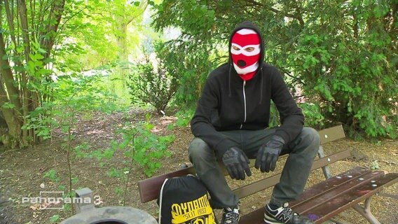 Mann mit Maske, der auf einer Bank sitzt.  