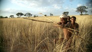 Buschjäger in der Kalahari-Wüste in Afrika schießen einen Giftpfeil mit Pfeil und Bogen auf eine Antilope.  