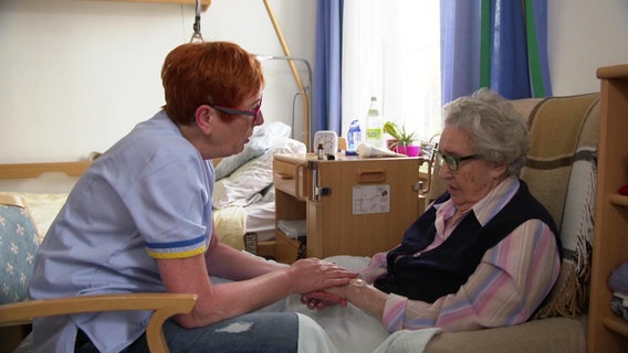 Pflegerin Elke Wernado streichelt einer älteren Dame die Hände.  