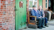 Zwei ältere Herren sitzen auf einer Bank.  