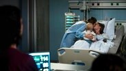 Eine Familie sitzt an einem Krankenhausbett.  