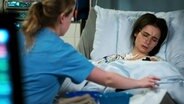 Mit schmerzverzehrtem Gesicht liegt eine Andrea Kirchner (Marina Frenk) im Krankenhausbett.  
