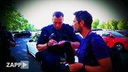 Polizist nimmt Personalien von Kameramann auf  
