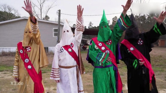 Mitglieder des Ku-Klux Klans heben die Hand.  