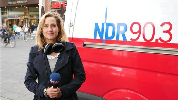 NDR 90,3 Stadtreporterin Anna Rüter steht mit einem Mikro in der Hand und Kopfhörer um den Hals vor einem Ü-Wagen.  