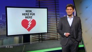 Christian Ehring moderiert extra 3, auf dem Bildschirm im Hintergrund steht "Ein Herz für Merz"  