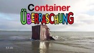 Ein gestrandeter Contaier auf Borkum. Auf dem Bild befindet sich die Aufschrift "Container Überraschung" im Stil vom "KINDER - Überraschungs-Ei".  