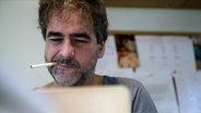 Deniz Yücel sitzt vor seinem Computer, eine Zigarette im Mundwinkel.  