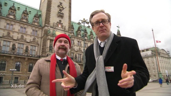 Ingo Wolski von der SPD (links) und Phillip Mayer-Degenhardt von der CDU stehen vorm Hamburger Rathaus und schauen in die Kamera.  