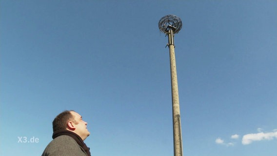 Eine Person schaut hoch auf ein Turm mit einem Nest.  