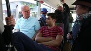 Ein älterer Mann sitzt neben einem dunkelhäutigen Mann im Bus.  