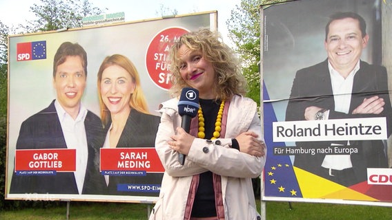 Eine Reporterin zwischen zwei Wahlplakaten.  