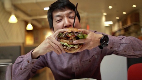 Reporter Han Park beißt in einen Burger mit Ersatzfleisch.  