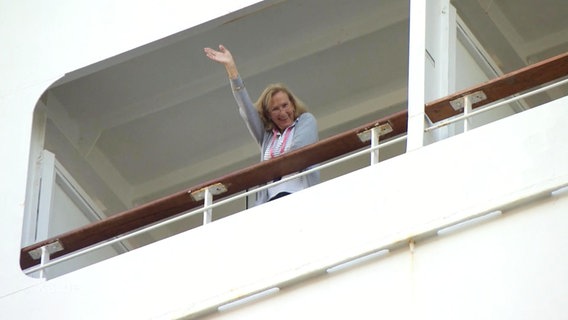 Eine Besucherin eines veganen Kreuzfahrtschiffs winkt von ihrem Balkon.  
