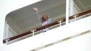 Eine Besucherin eines veganen Kreuzfahrtschiffs winkt von ihrem Balkon.  