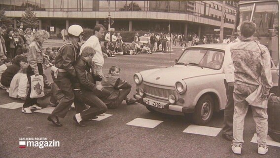 Ein Foto von Aram Radomski zeigt Protestierende auf der Straße sitzend in der DDR.  