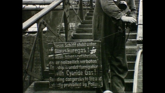 Ein historisches Schild vor einem Schiff auf dem steht, dass man das Schiff wegen eines Blausäuregases nicht betreten darf. © NDR 