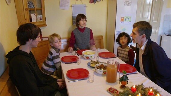 Eine Familie - Vater, Mutter und drei Kinder - sitzen am Tisch.  