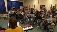 Eine Klasse spielt zusammen mit der NDR Big Band in einem Klassenzimmer einer Schule.  