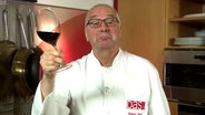 Rainer Sass mit einem Glas Rotwein in der Hand.  