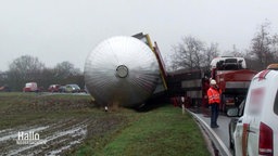 Ein Gastank liegt umgekippt auf einem Acker, daneben ist die Ladefläche des Schwertransporters zu sehen.  