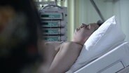 Ein Mann liegt scheinbar bewusstlos in einem Krankenhausbett (nachgestellte Szene).  