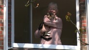 Ulrike Kropp steht an einem offenen Fenster ihres Hauses und trägt ihre Hauskatze auf dem Arm.  