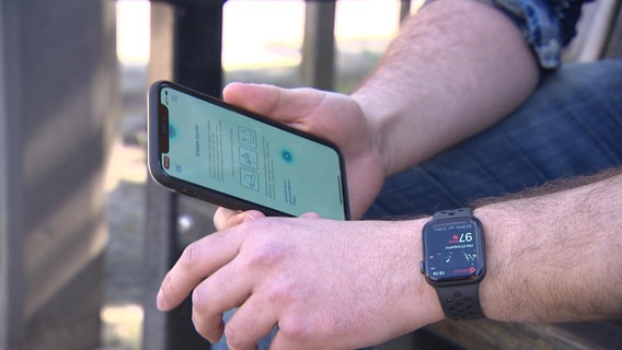 Man trägt eine Smartwatch und hat auf Smartphone die Corona-Datenspende-App geöffnet.  