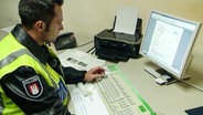 Ein Polizist sitzt vor einem sehr alten PC.  