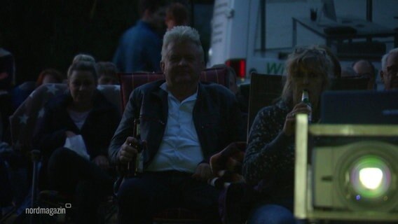 Menschen sitzen im Open-Air Kino hinter einem Projektor.  