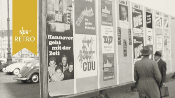 Zwei Passanten vor einer Plakatwand mit Werbung verschiedener Parteien  
