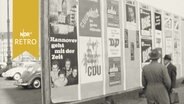 Zwei Passanten vor einer Plakatwand mit Werbung verschiedener Parteien  