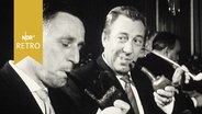 Zwei Herren mit Pfeifen in einer Saalveranstaltung  