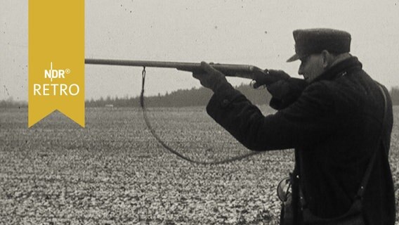 Jäger legt mit Schrotflinte an, auf einem verschneiten Acker stehend  