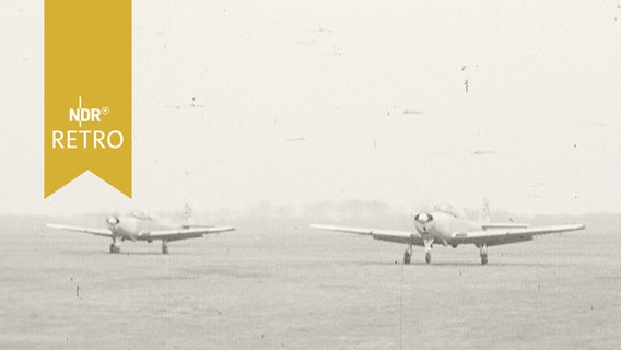Zwei Propellerflugzeuge auf einer Wiese nebeneinander  