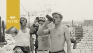 Drei Maurer trinken Bier aus der Flasche auf einer Baustelle  