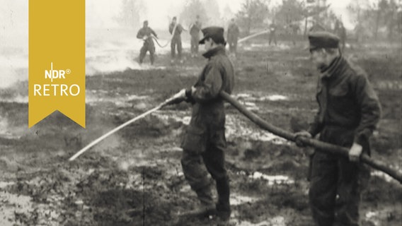 Zwei Helfer in Uniform halten einen Schlauch beim Löschen von Moorbrand  